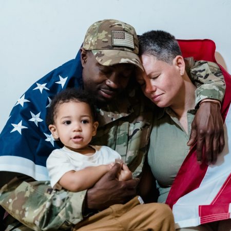 Military family embracing while wrapped in an American flag